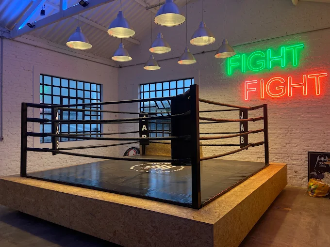 Ringue de boxe da JAB L.U.T.A.S com letreiro neon FIGHT ao fundo